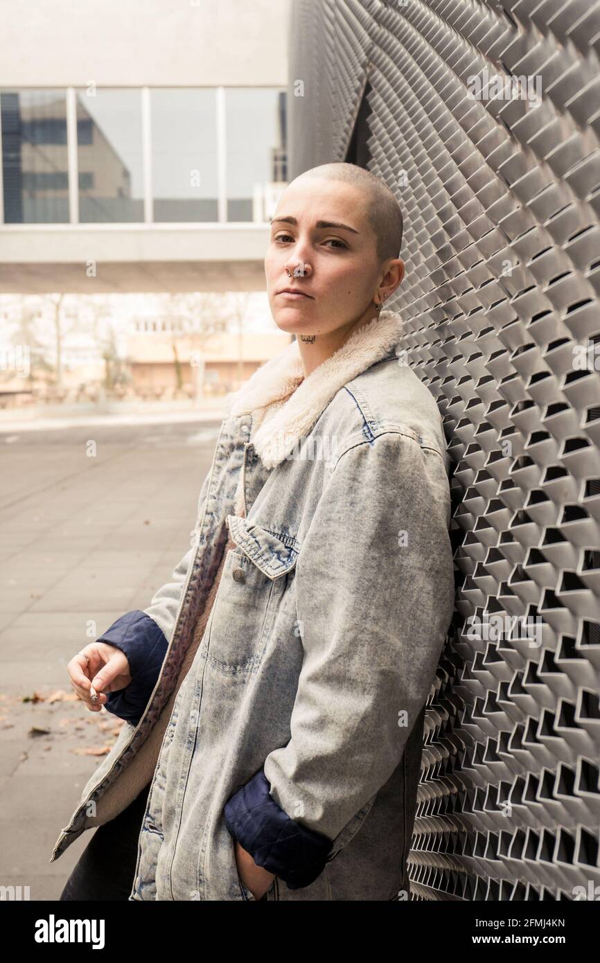 Side view of self confident young transgender person in denim jacket smoking cigarette while looking at camera Stock Photo