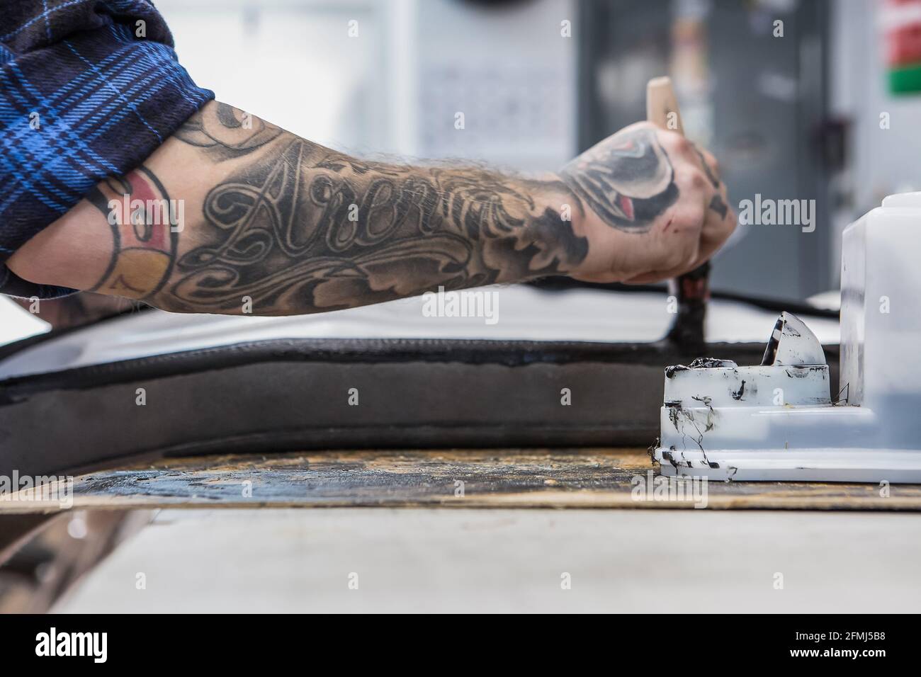 Crop side view of tattooed craftsman applying glue on motorcycle seat
