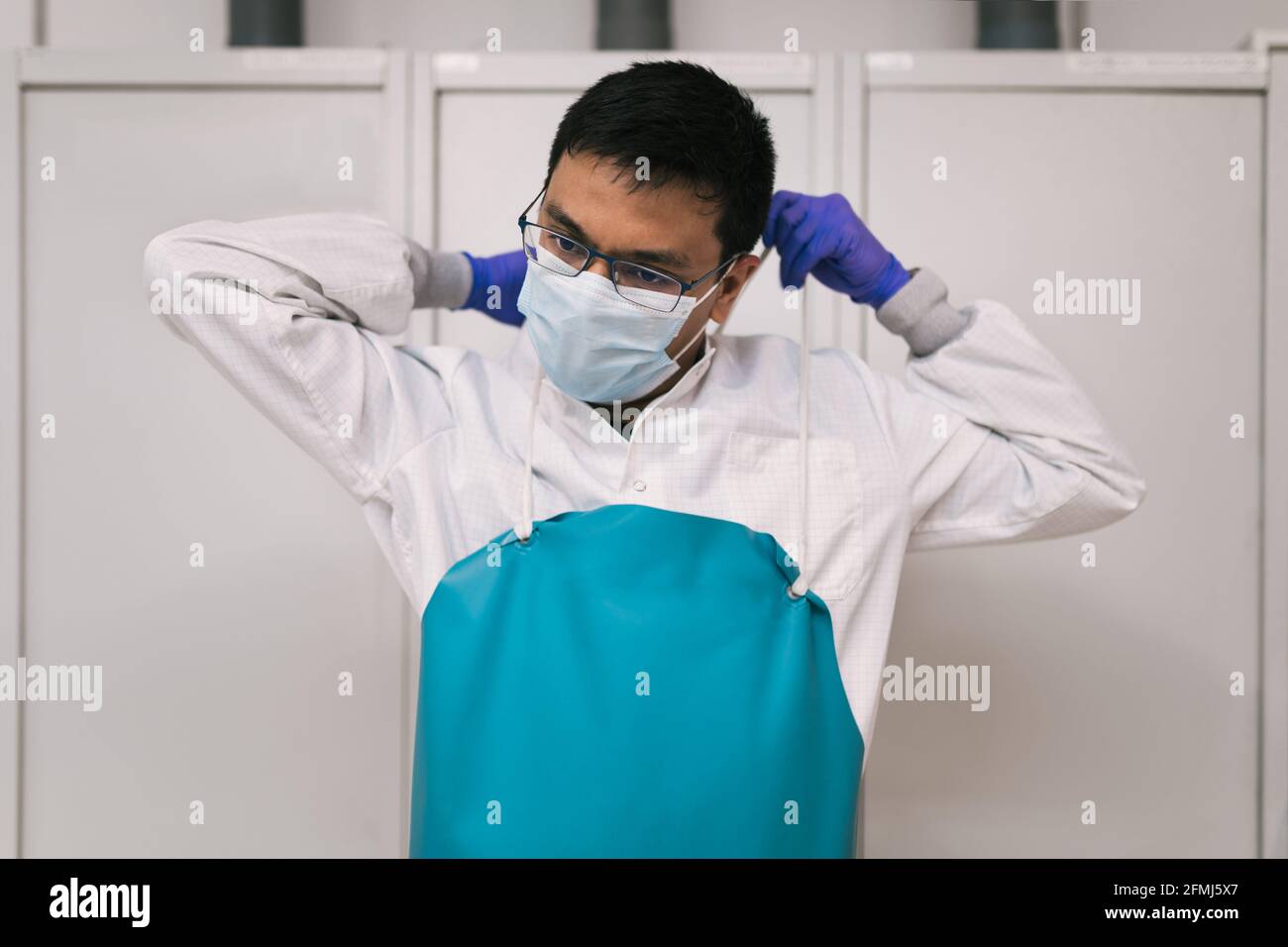 Serious ethnic male doctor in white robe gloves and face mask putting