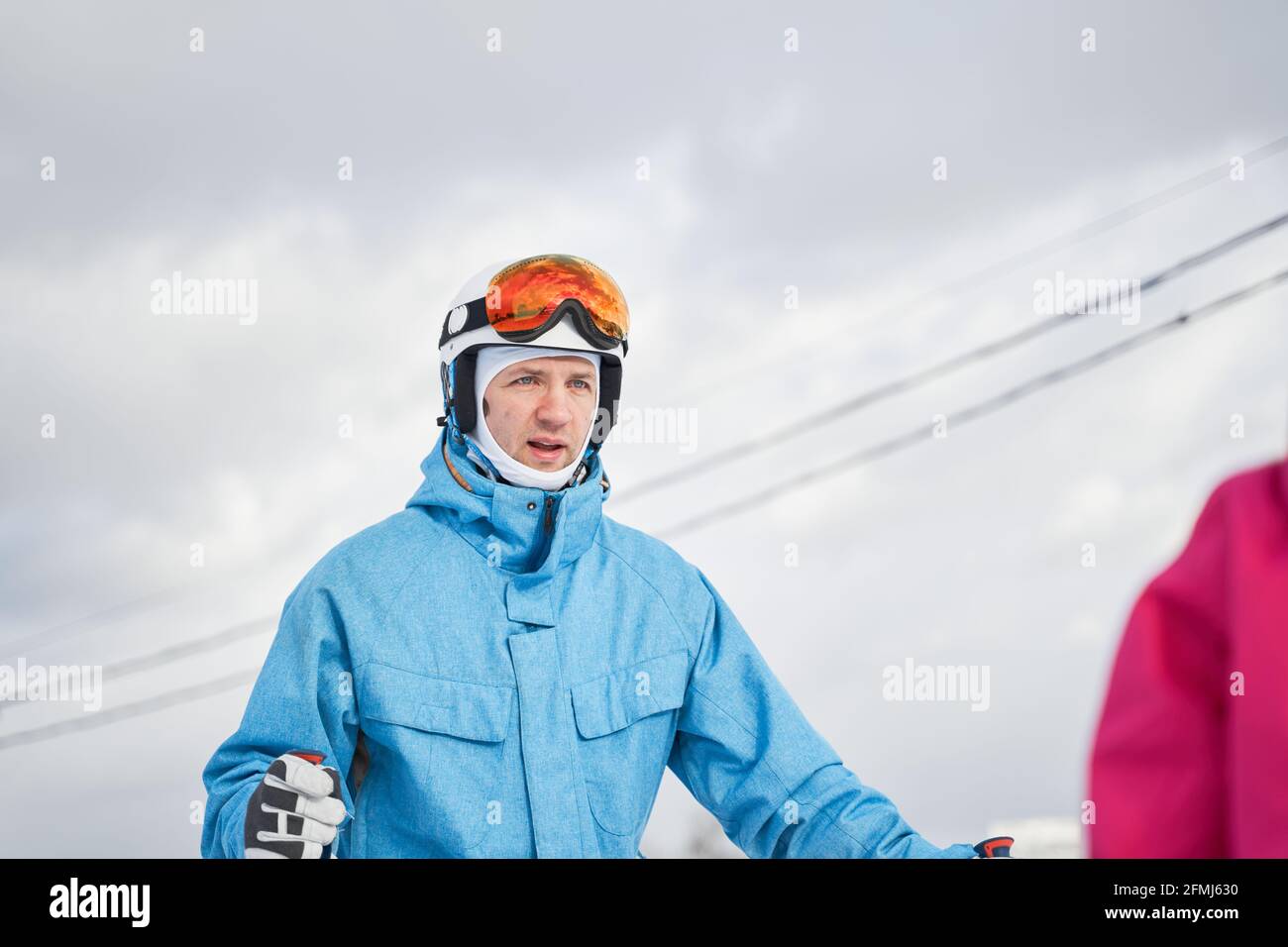 Glad father and crop daughter wearing warm sports clothes and helmets standing with skis on snowy hill slope and looking away contentedly Stock Photo