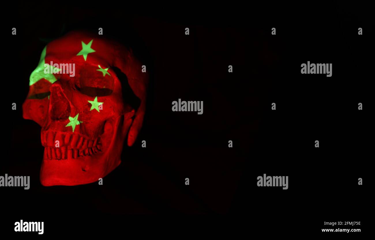 A confronting powerful image of a skull with the chinese national flag projected over it. Plain dark black background. Stock Photo