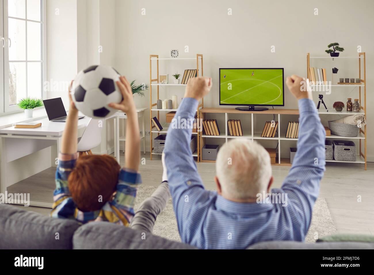 Grandfather and grandson sitting on sofa, watching soccer and supporting favorite team Stock Photo