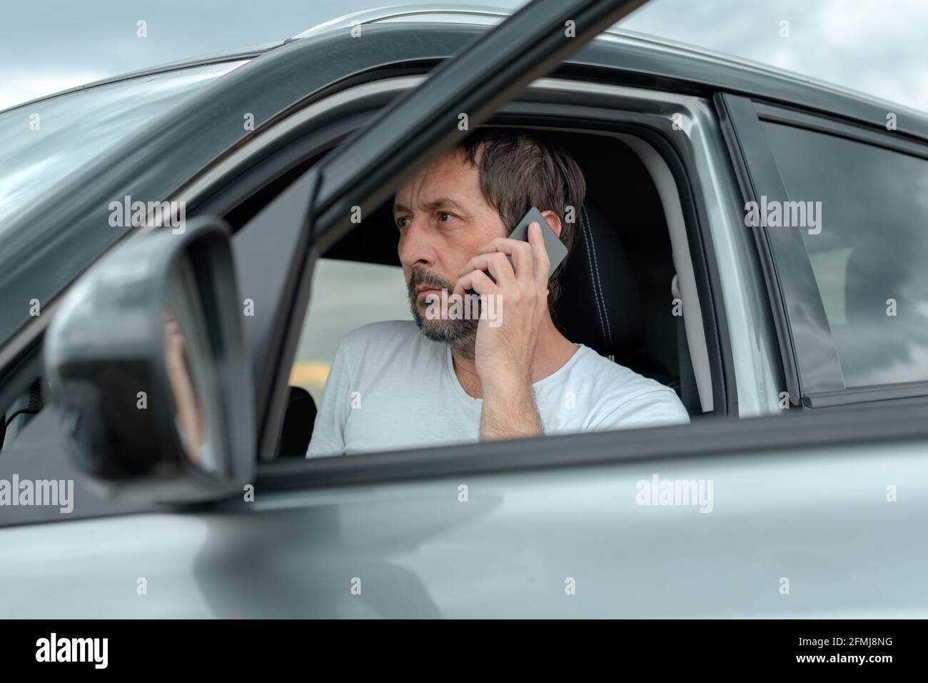 Adult man sitting in car and talking on mobile phone, looking serious and worried, selective focus Stock Photo