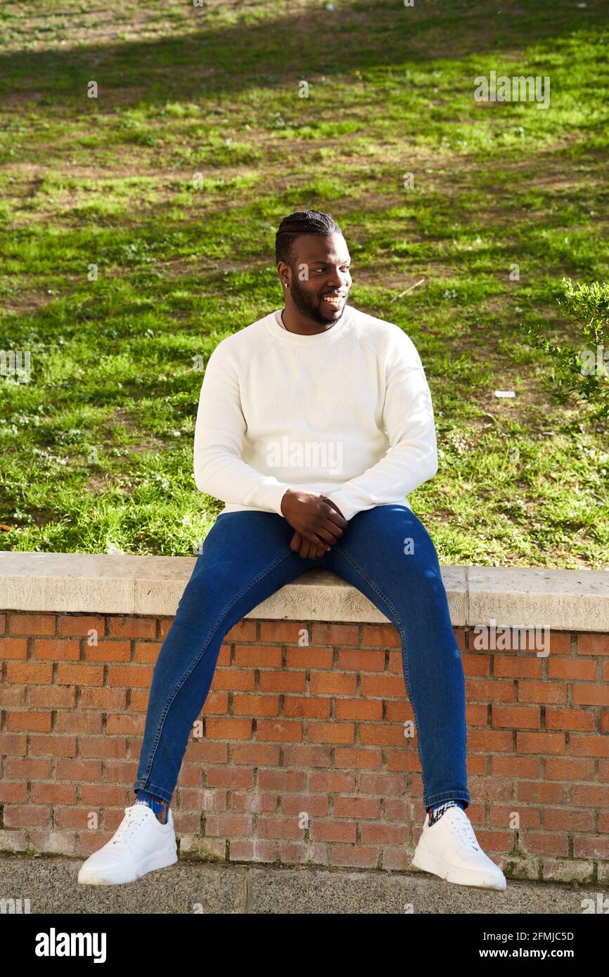 Young African American man smiling sitting on a wall. Happy Latino man. High quality photo Stock Photo