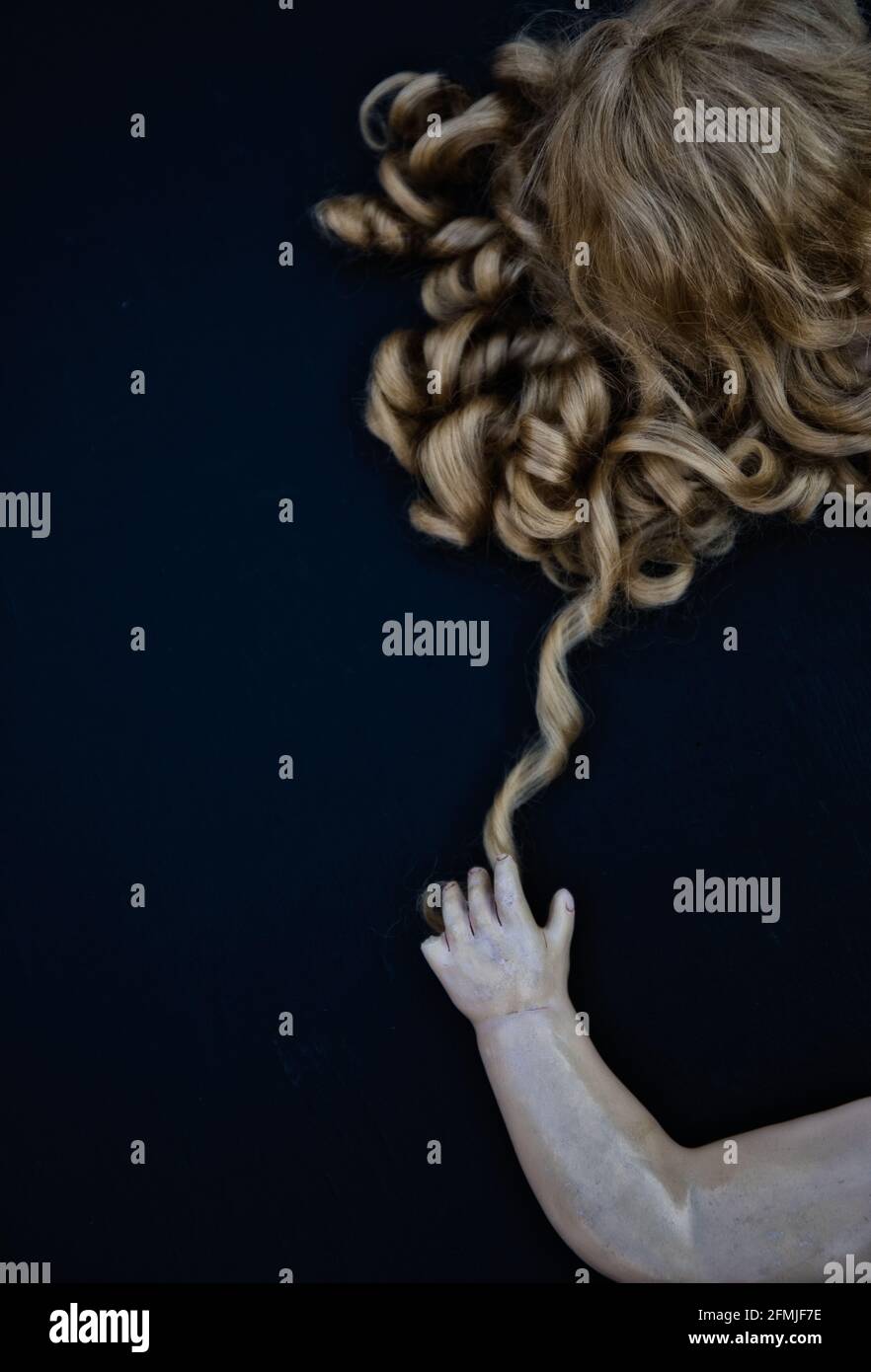 Directly above of ceramic dolls hand touching dolls curly wavy hair against black background. Concept of strange,different, curiosity,intrigue Stock Photo