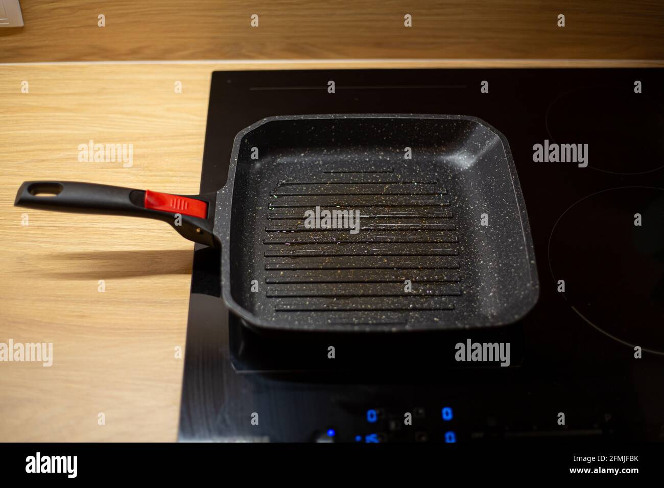 Black oily grill pan is heating on electrical ceramic hob for burger