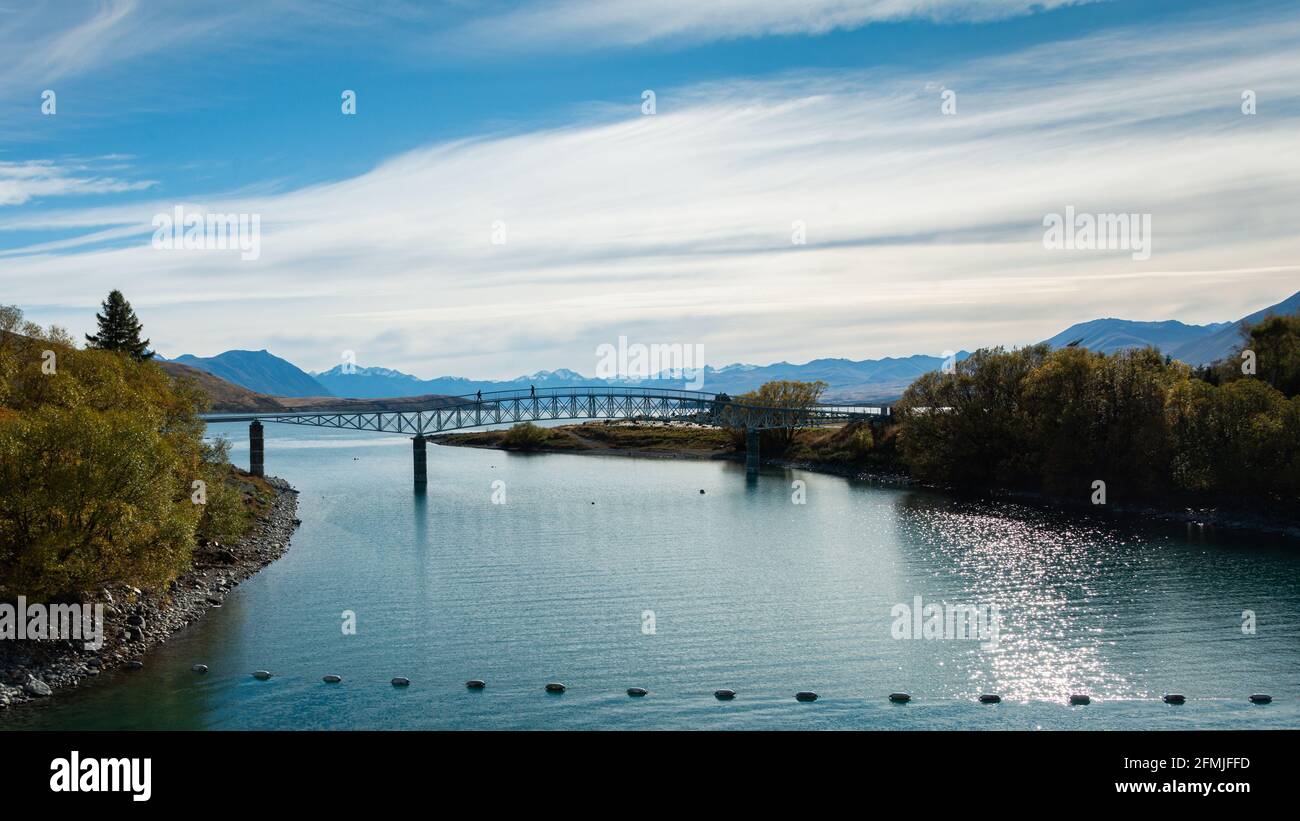 Panorama view of Lake Tekapo with the Southern Alps in the background and people walking on the Footbridge, South Island Stock Photo