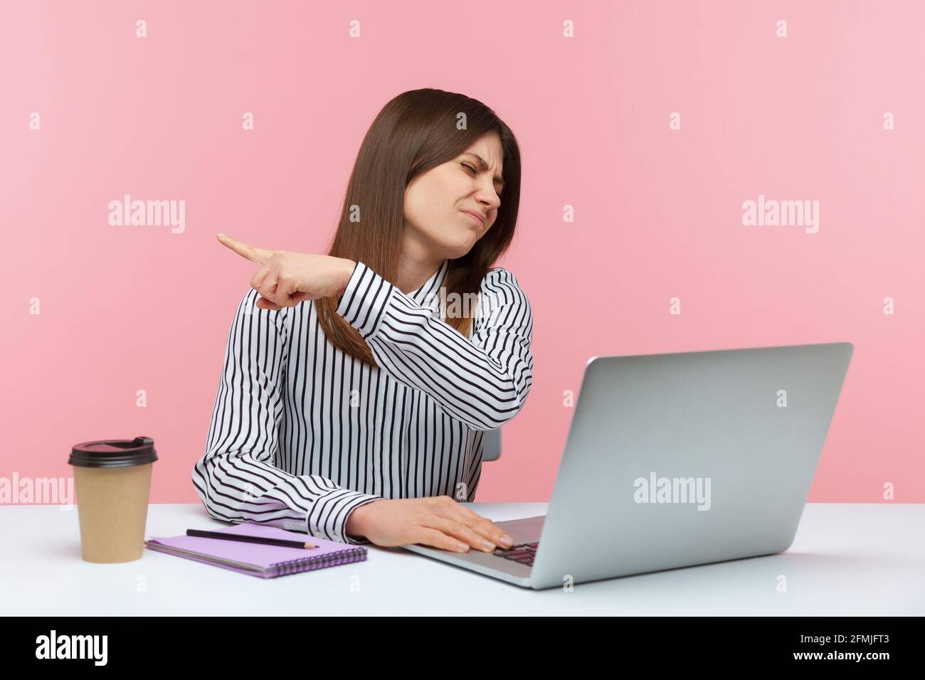 Irritated bossy business woman sitting at workplace and pointing finger aside showing exit, asking to leave office, firing from work. Indoor studio sh Stock Photo