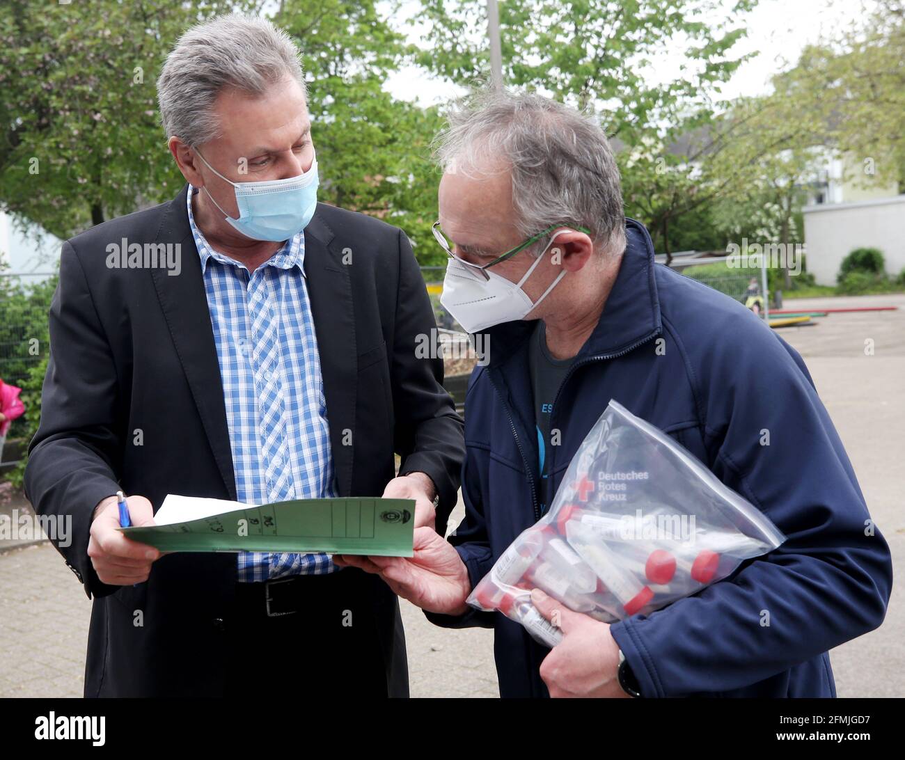 10 May 2021, North Rhine-Westphalia, Essen: Udo Moter (l), headmaster of Maria-Kunigunda primary school, hands over the list and the collected pool sample tubes with 'lollipop tests' to the lab driver. North Rhine-Westphalia is introducing so-called Lolli tests across the board at all elementary and special schools on Monday. With the test, all more than 730,000 pupils of the almost 3,800 primary and special schools will be tested twice a week in their respective learning groups for the coronavirus. Photo: Roland Weihrauch/dpa Stock Photo