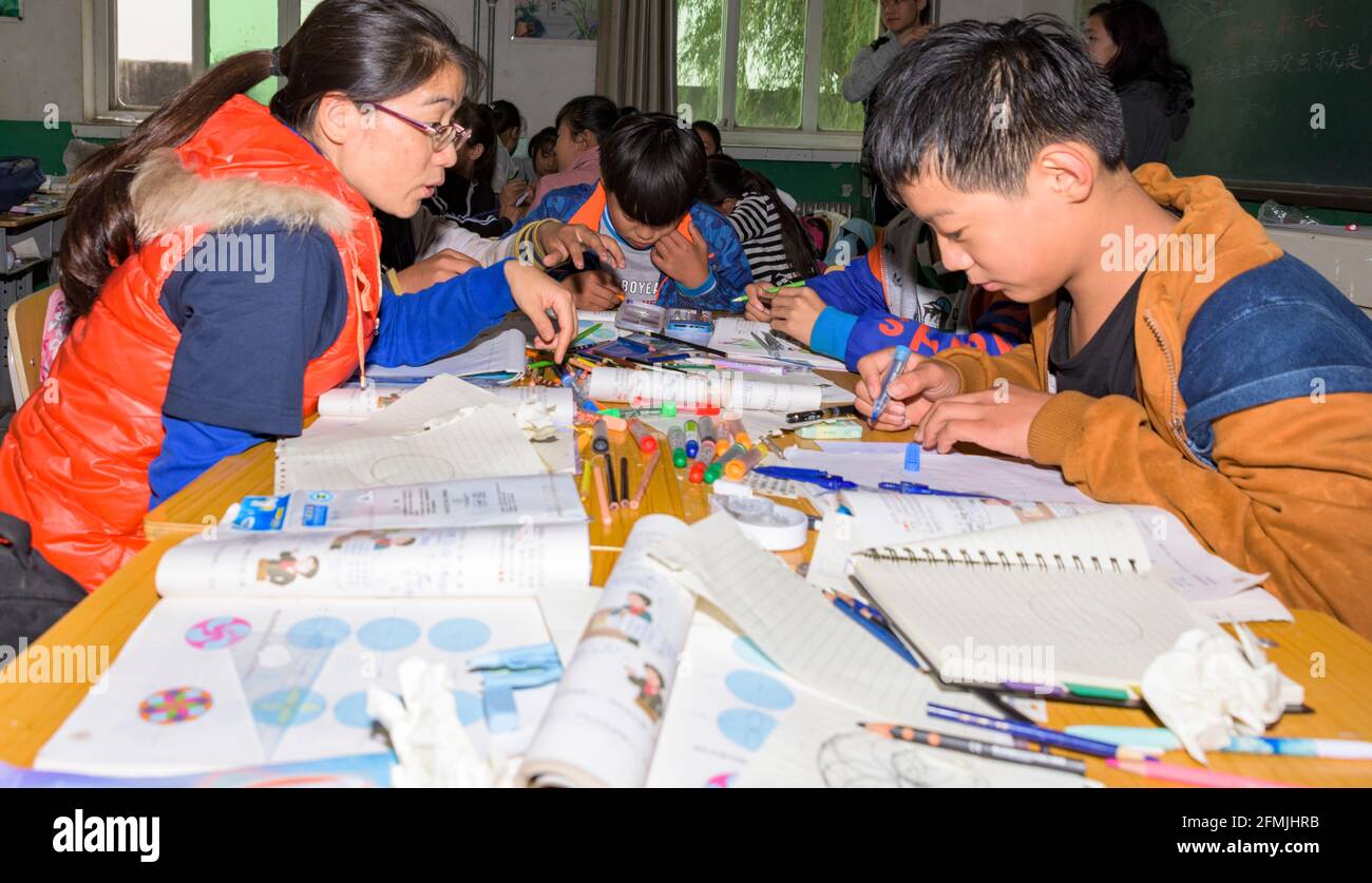 The teacher assists students at Xilain Primary school in Hebei with their classwork. Stock Photo