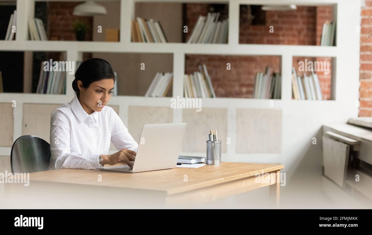 Confident Indian businesswoman working on laptop, sitting at desk Stock Photo