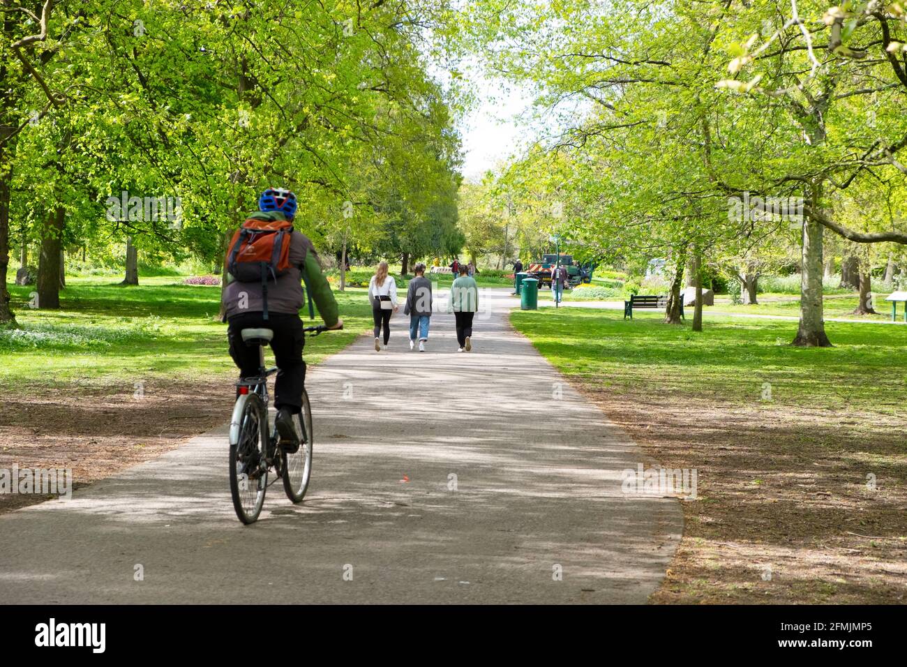 Rear back view of cyclist with rucksack cycling riding bike bicycle on cycle path in Bute Park young women walking Cardiff Wales UK   KATHY DEWITT Stock Photo