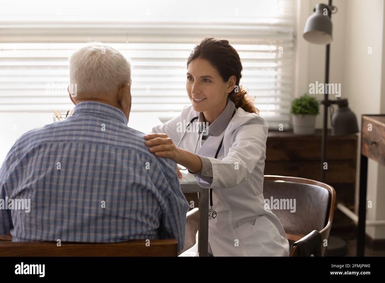 Smiling female doctor touch elderly male shoulder reassure give hope Stock Photo