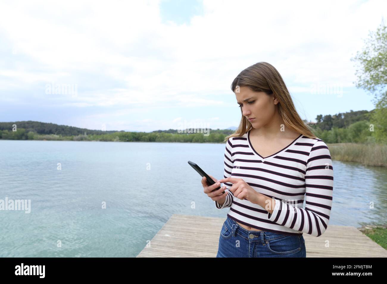 Sad woman reading message on smart phone on vacation in a lake Stock Photo