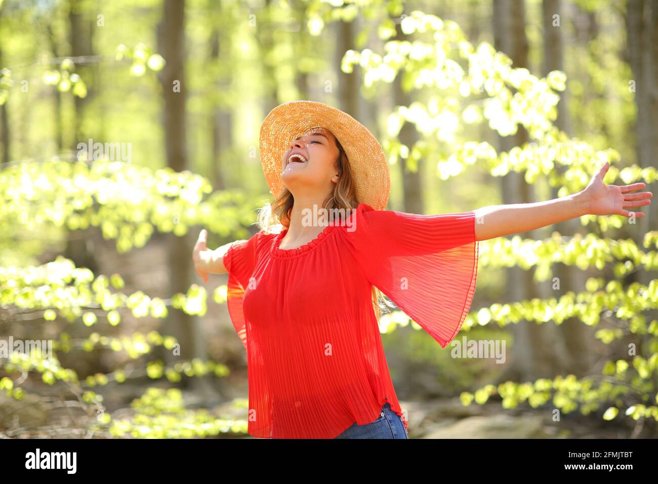 Excited woman spreading happiness outstretching arms in a green forest ...