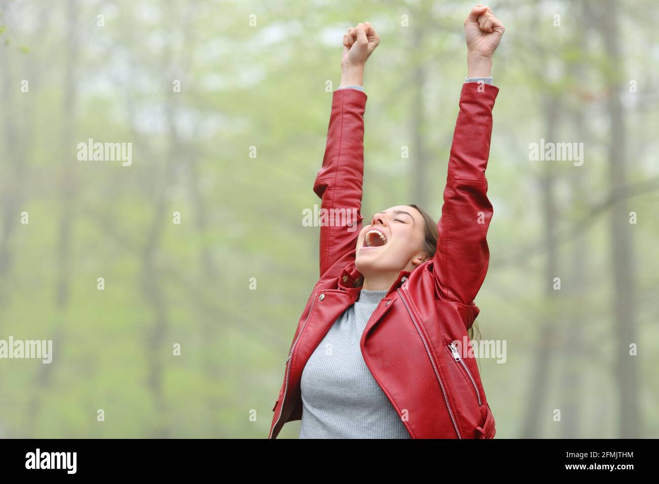 Woman in red excited raising arms screaming in a forest Stock Photo