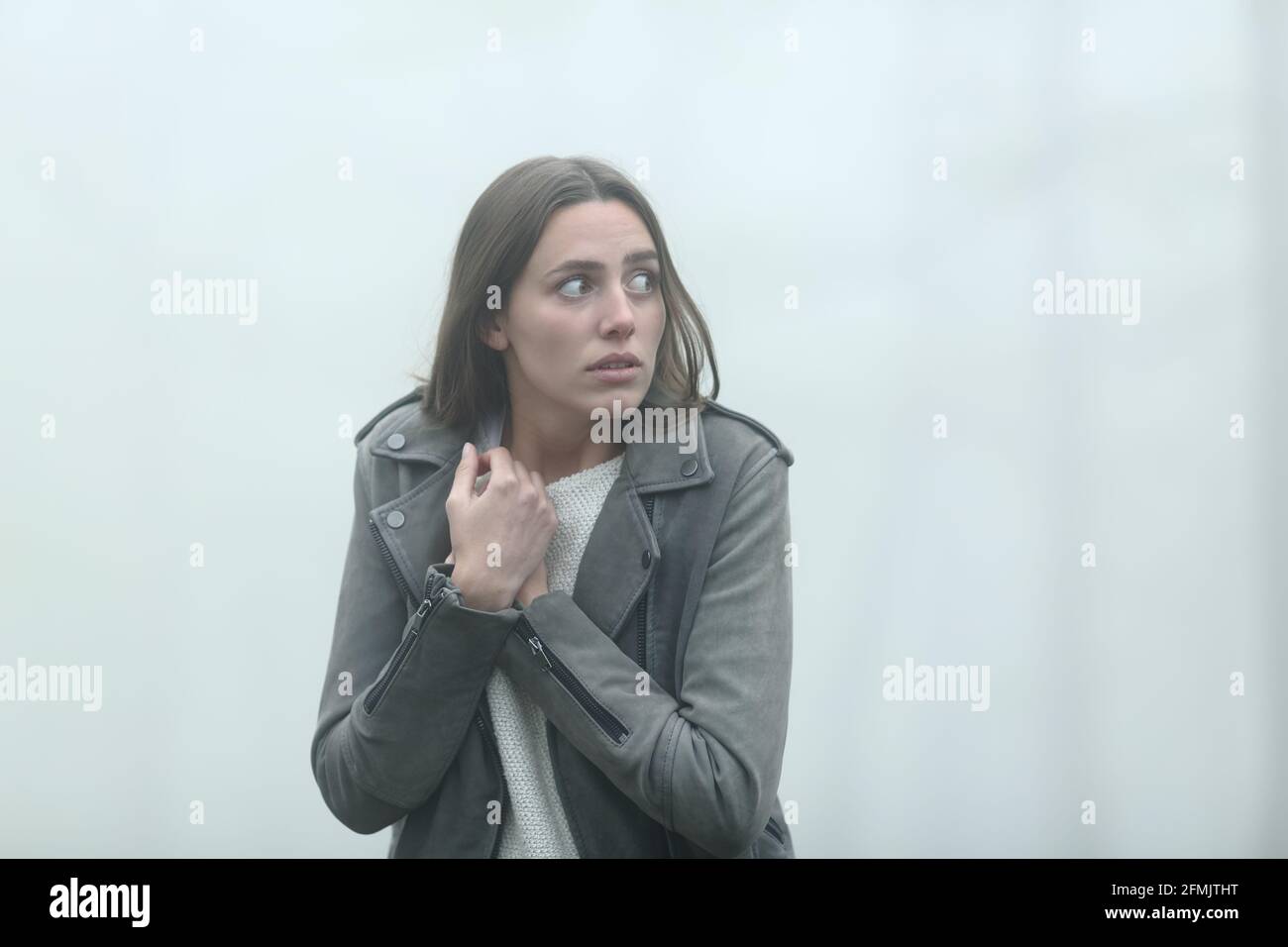 Scared casual woman walking alone looking at side in a foggy park Stock Photo