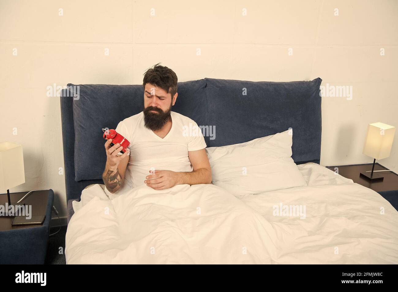 Its hard to get out of bed. Bearded man check time with alarm clock. Sleep time. Sleep and wake routine. Bed time. Bedtime. Morning and night. Regular Stock Photo