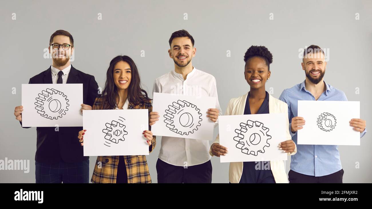 Group portrait of happy diverse business people holding pictures of different gears Stock Photo