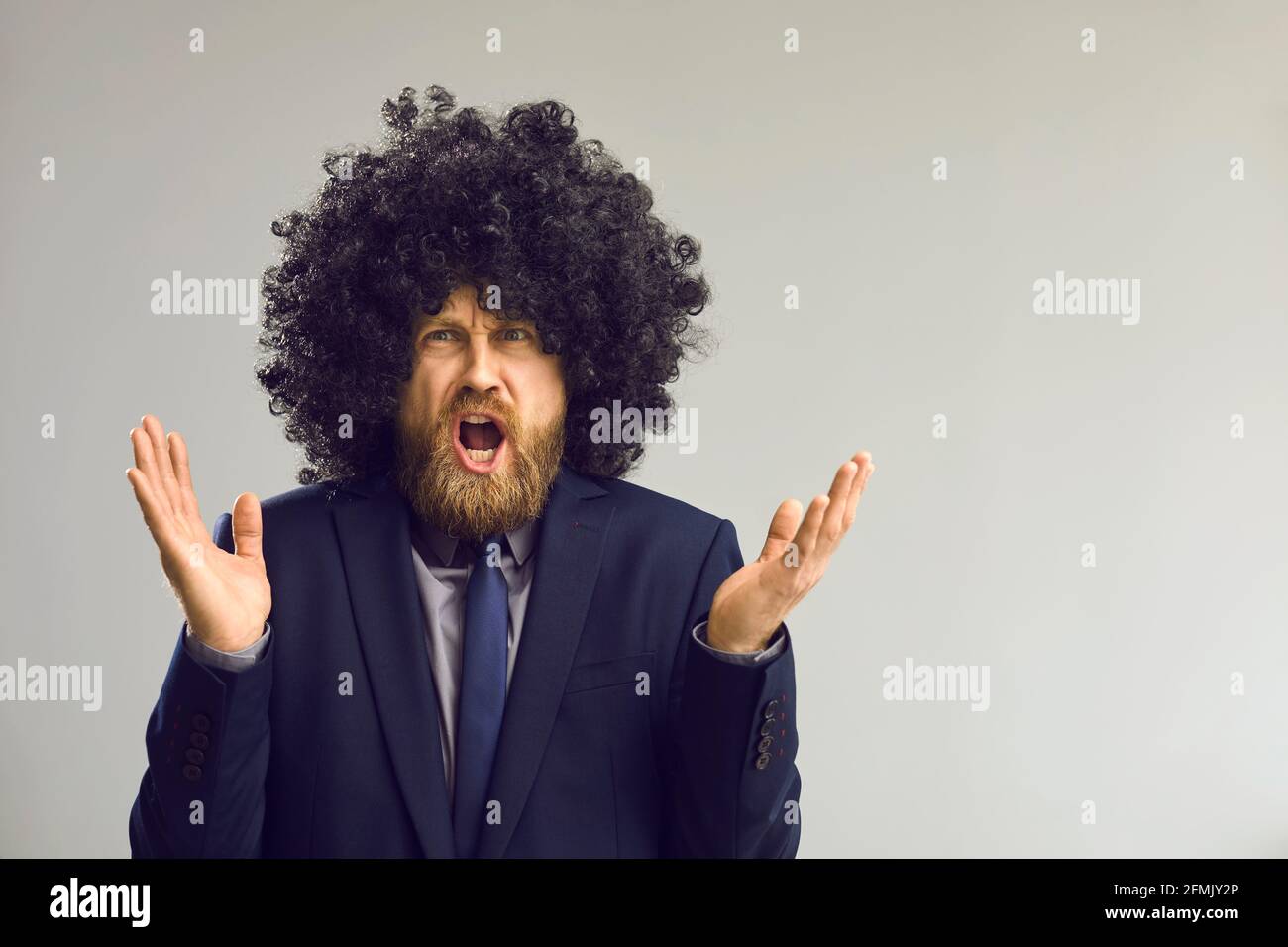 Funny man in afro hair wig angry shouting and gesturing at camera studio shot Stock Photo