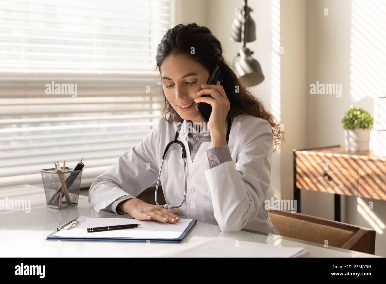 Confident latin female gp counselling caller by phone from office Stock Photo
