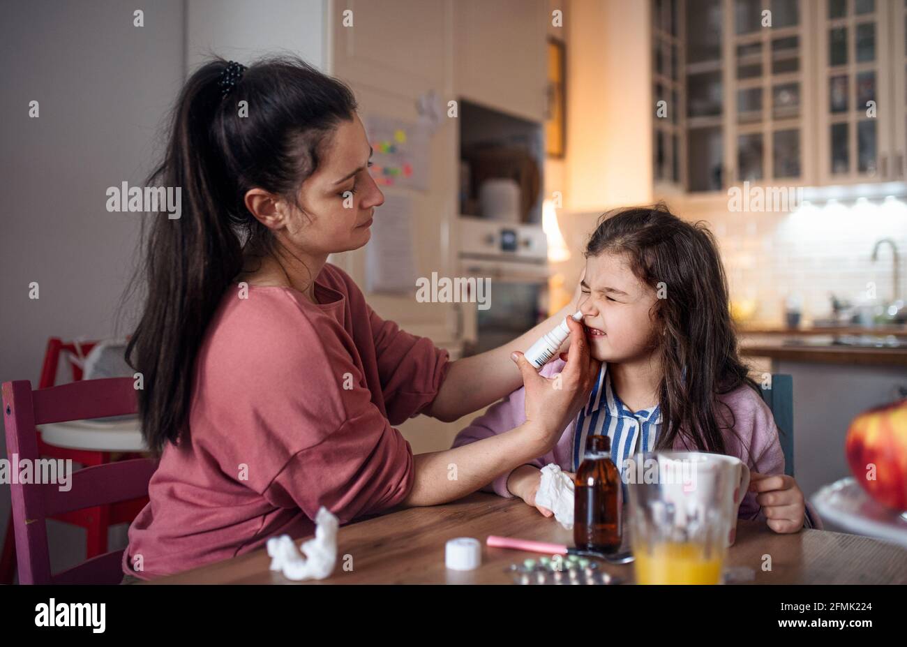 Mother looking after sick small daughter at home, using nasal spray. Stock Photo