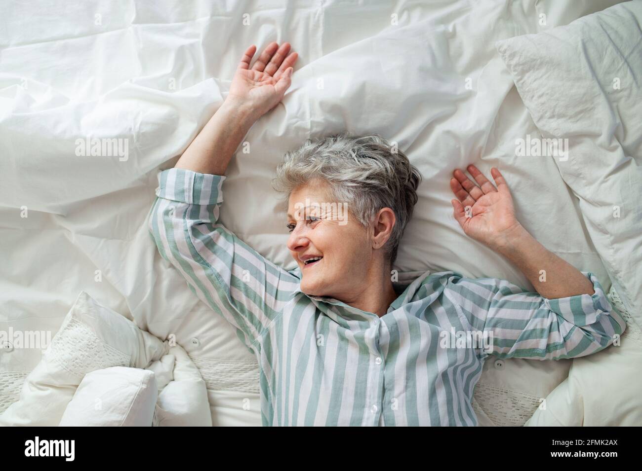Top view of happy senior woman in bed at home, relaxing. Stock Photo
