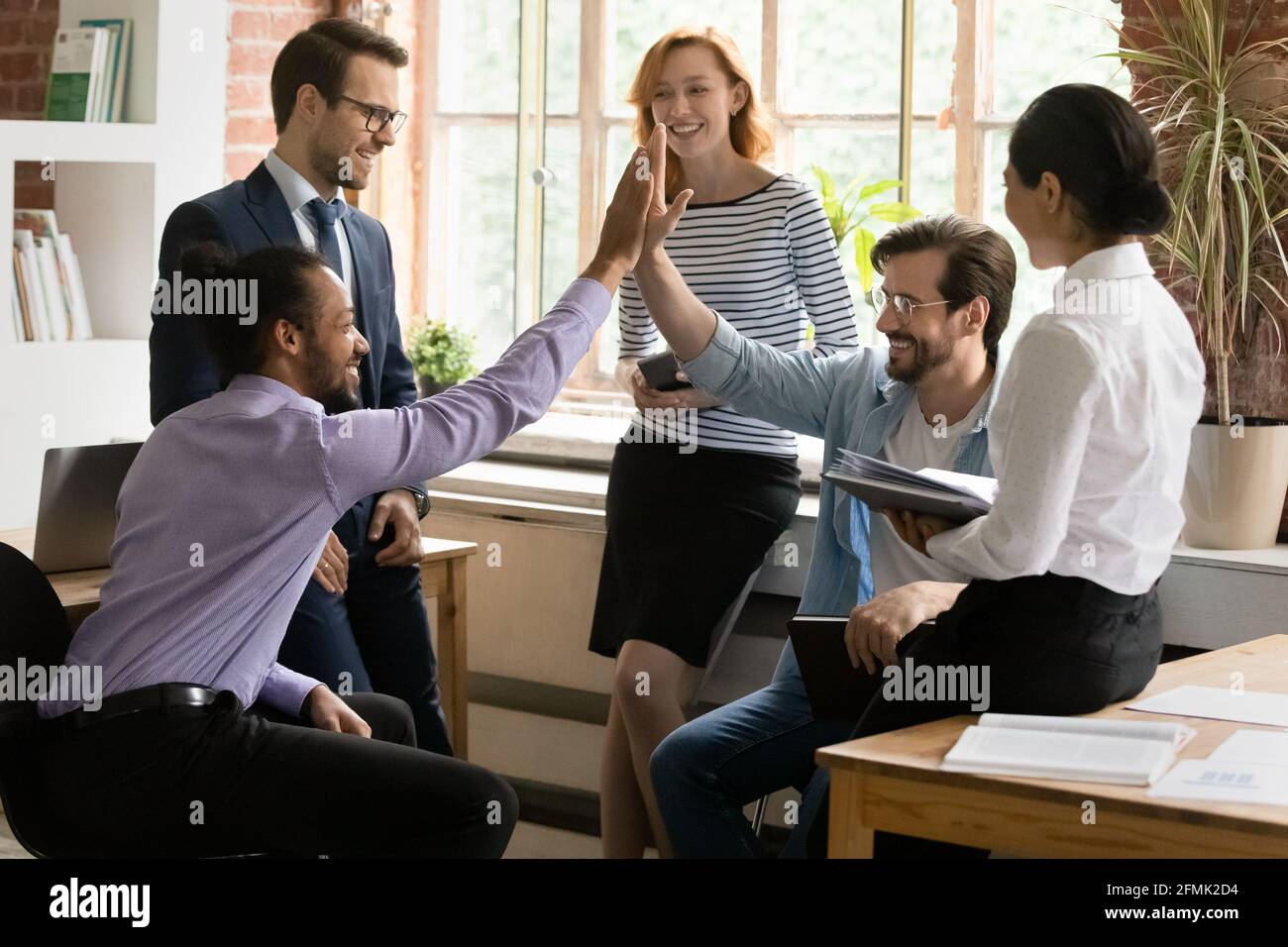 Excited diverse colleagues giving high five at meeting, celebrating ...