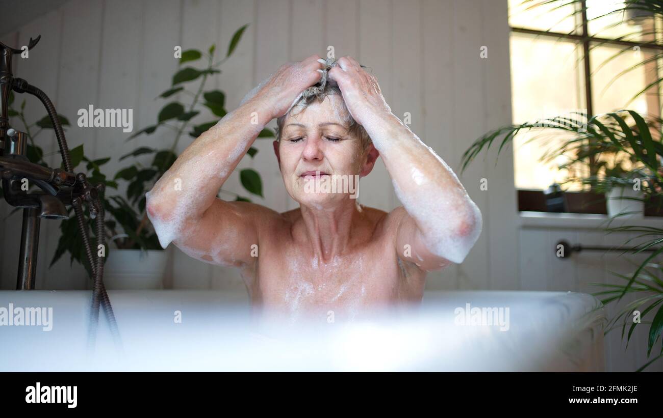 Contented senior woman washing in bubble bath tub at home, eyes closed. Stock Photo