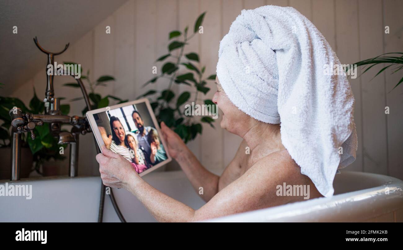 Senior woman with tablet in bath tub at home, video call with daughter and grandchildren. Stock Photo