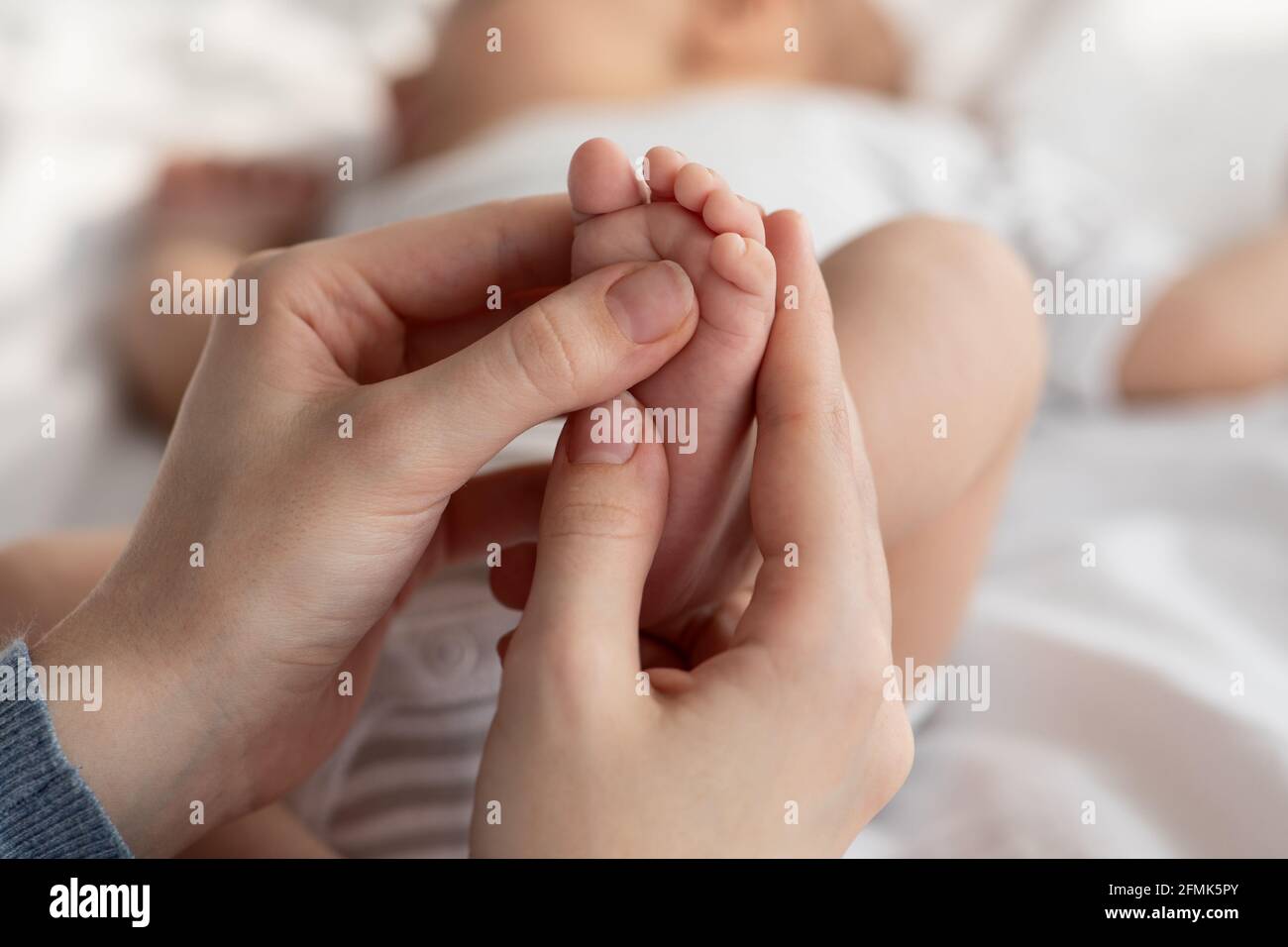 Closeup Shot Of Caring Mother Massaging Her Newborn Baby's Foot, Unrecognizable Loving Mom Making Strengthening Gymnastic Exercises For Her Sleeping I Stock Photo