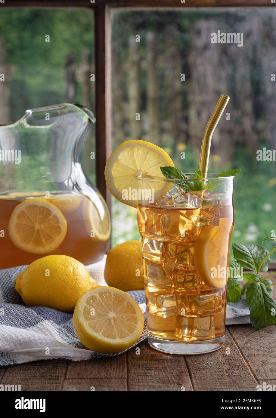 Glass of iced tea with lemon and mint on a wooden table by a window ...