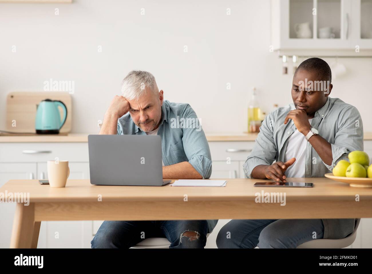 Problems with taxes, bills and deductions, debts and credit. Sad adult african american and elderly european men talking, working with documents, tabl Stock Photo