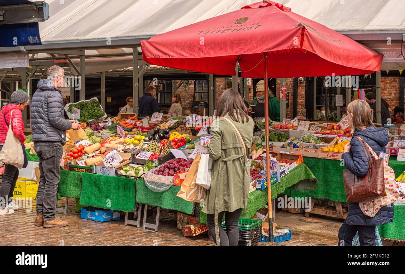 Market stall selling fruit and vegetables.  A customer is being served  and other shoppers look at the stall. Stock Photo