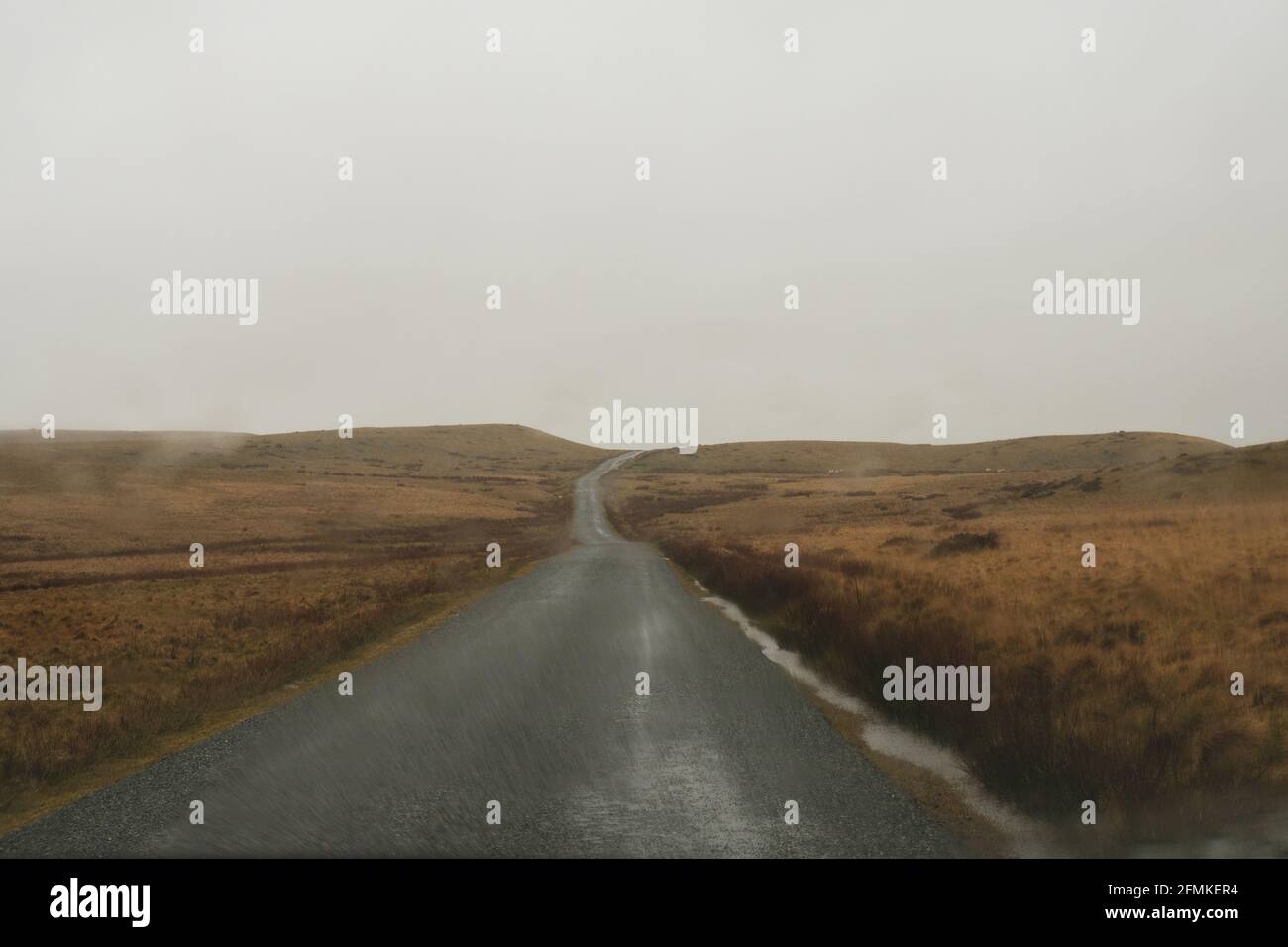 Looking through a car windscreen out onto a mountain road going across bleak moorland on a wet stormy day. With rain drops  on the window. Stock Photo
