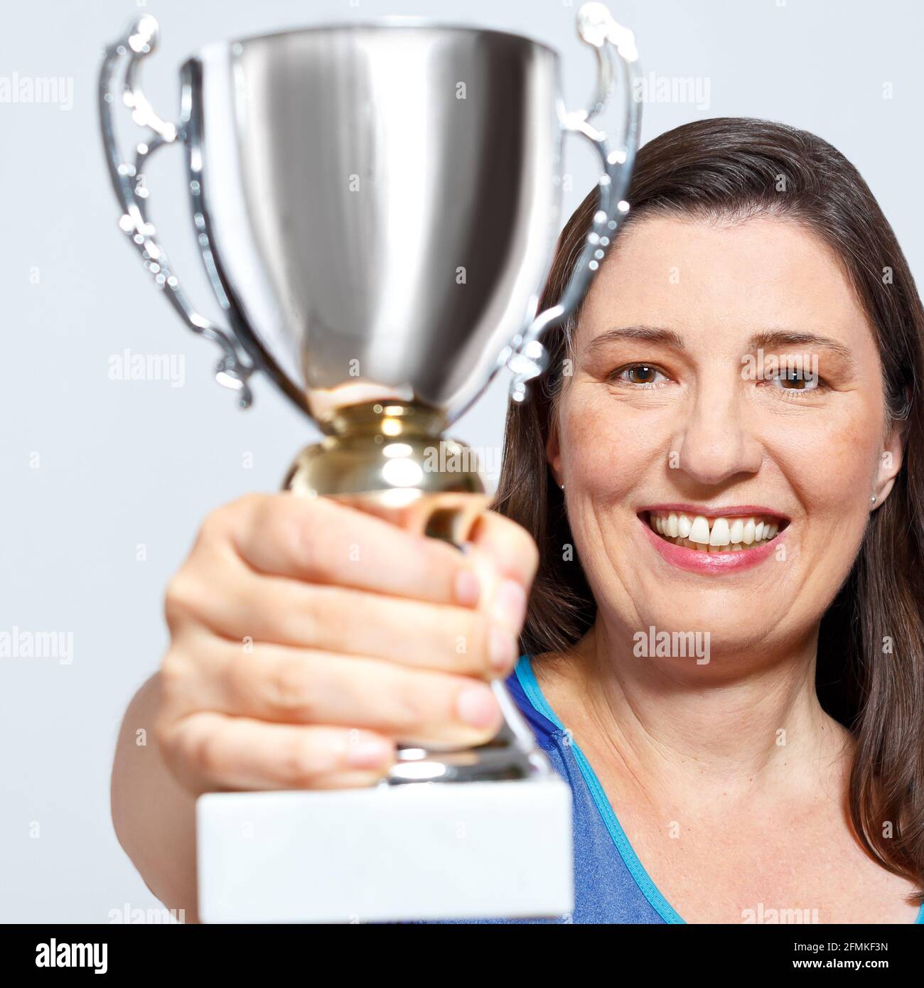 Proud smiling middle aged woman holding up a silver cup trophy, enjoying her sports achievement. Stock Photo