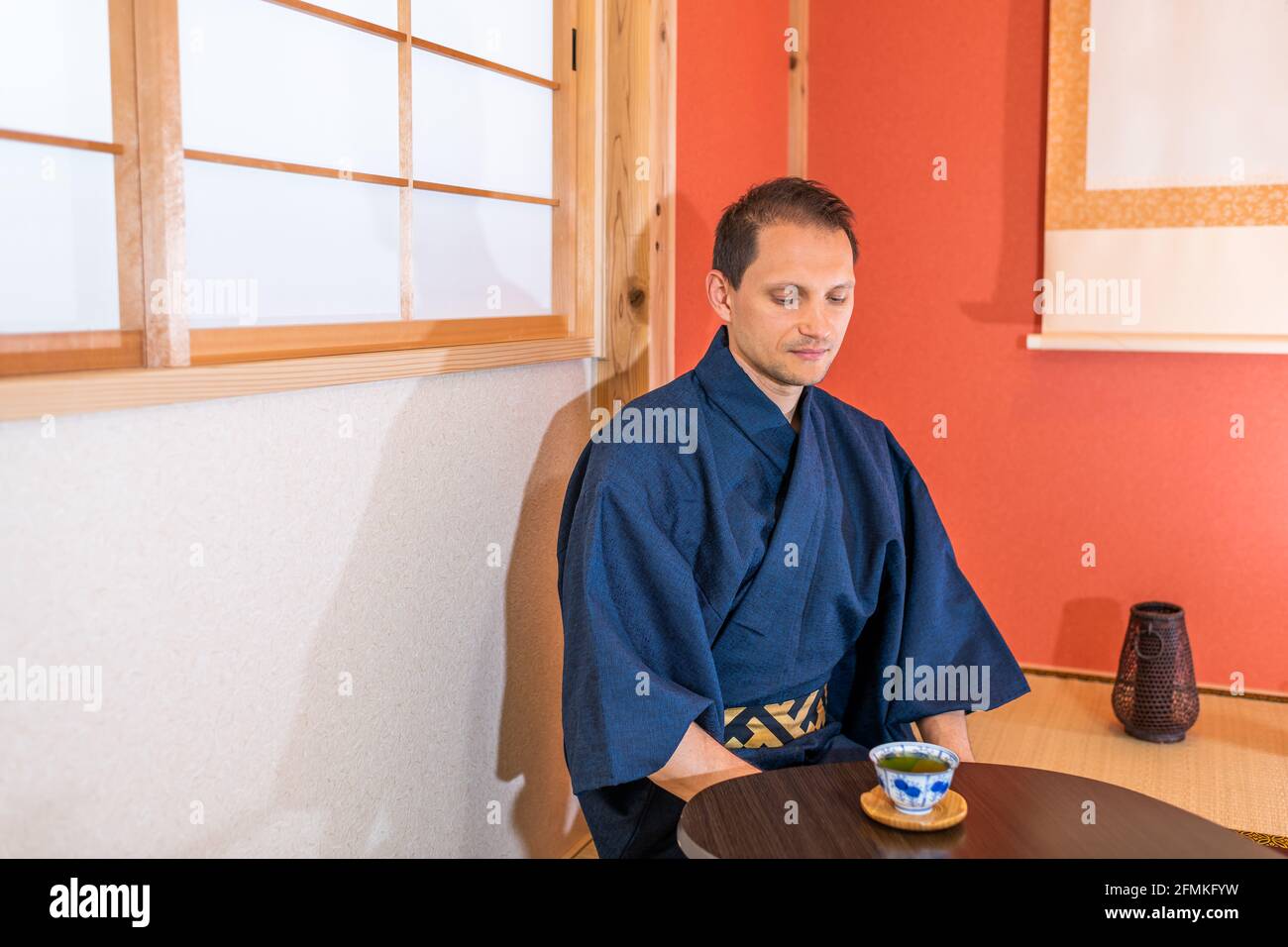 Traditional japanese house machiya ryokan with man in kimono by alcove and hanging paper scroll drinking green tea Stock Photo