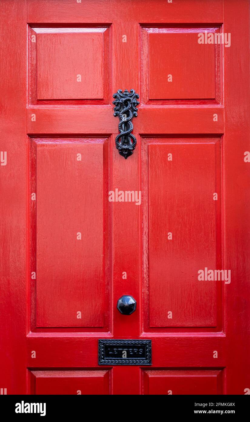 Ornate iron door knocker on a red wooden front door with black handle