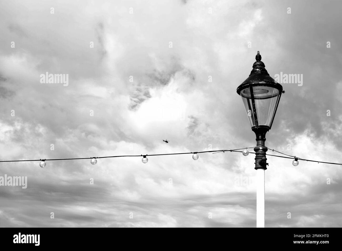 An old vintage street lamp and string lights along the promenade of a Victorian seaside town in Wales with moody cloudy sky Stock Photo