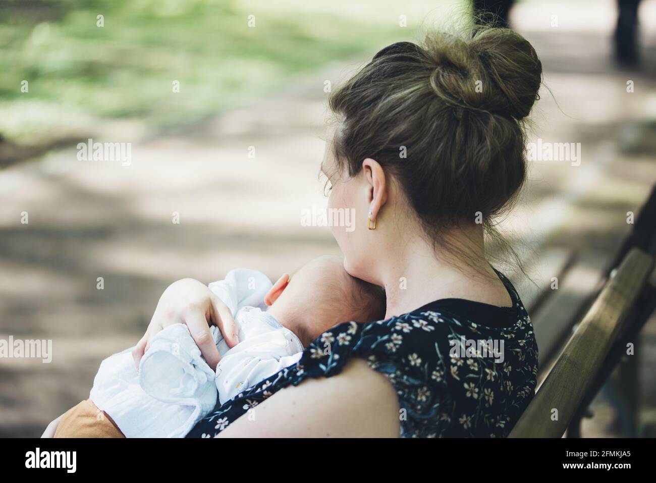 mother holding her baby in her arms on bench in park on a sunny summer day Stock Photo