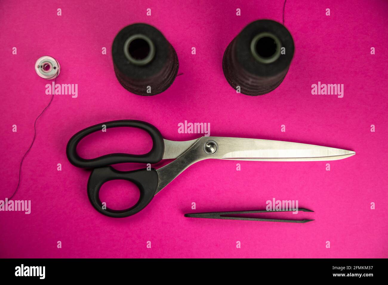Black tailoring accessories as scissors, thread, tweezers and bobbin on pink background Stock Photo