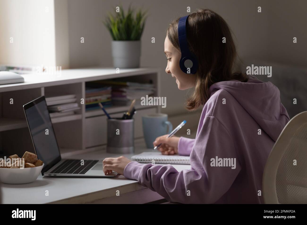 Smiling young teen schoolgirl in headphones holding video call. Stock Photo