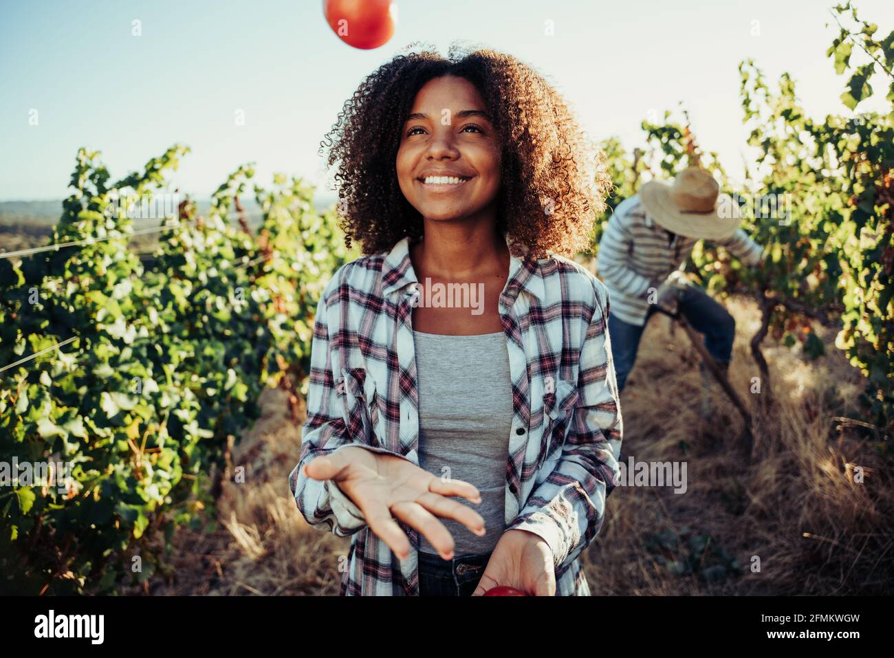 Mixed race female farmer playing with vegetables standing in vineyard  Stock Photo