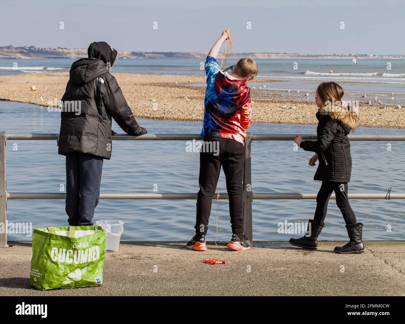 The Back Of Three Children Hunting For Shore Crabs, Crabbing At Mudeford Quay UK Stock Photo