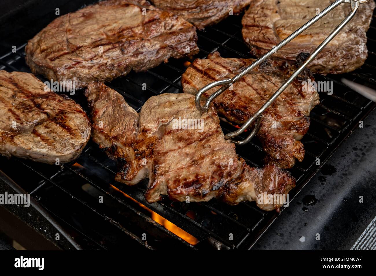 Tongs turning steaks cooking over a flame grill. Shot shallow depth of field Stock Photo Alamy