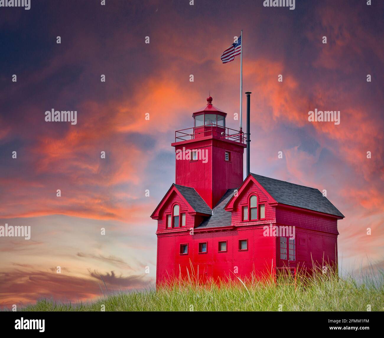 Red Michigan lighthouse in green dune grass and sunset sky Stock Photo