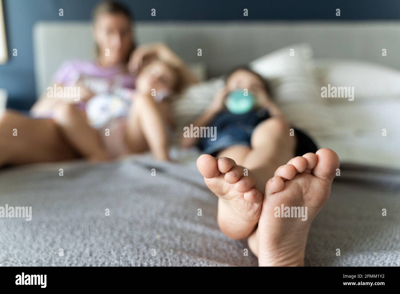 Kid barefoot lying on bed drinking millk next to anonymous mom and little  sister on blurry background. Feeling cozy at home concept Stock Photo -  Alamy