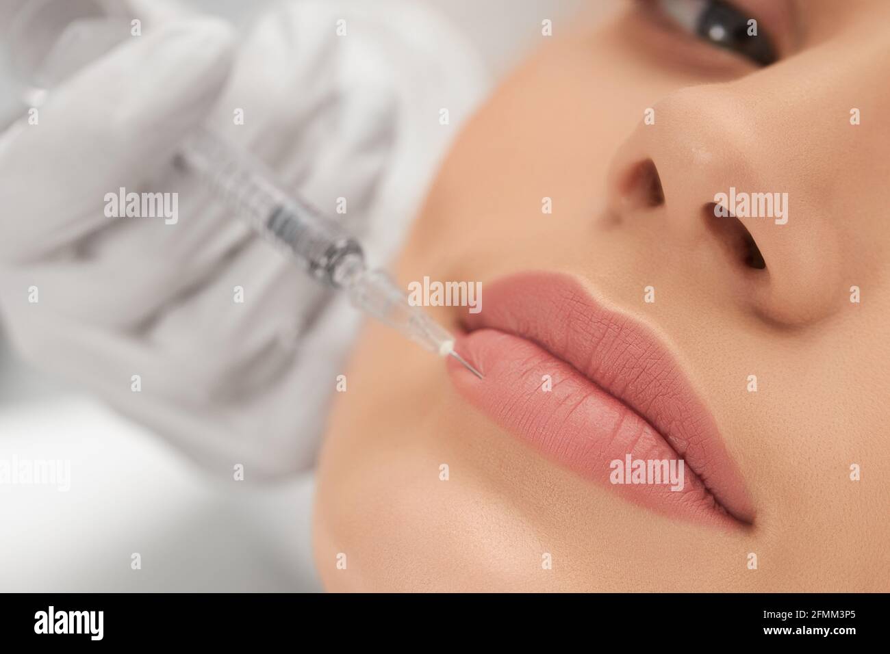 Close up of young attractive woman lying on procedure for lip augmentation in beautician. Concept of beauty procedure with good mood and with professional cosmetics. Stock Photo