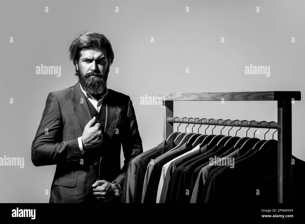 Male suits hanging in a row. Men clothing, boutiques. Tailor, tailoring. Stylish men's suit. Man suit, tailor in his workshop. Black and white Stock Photo