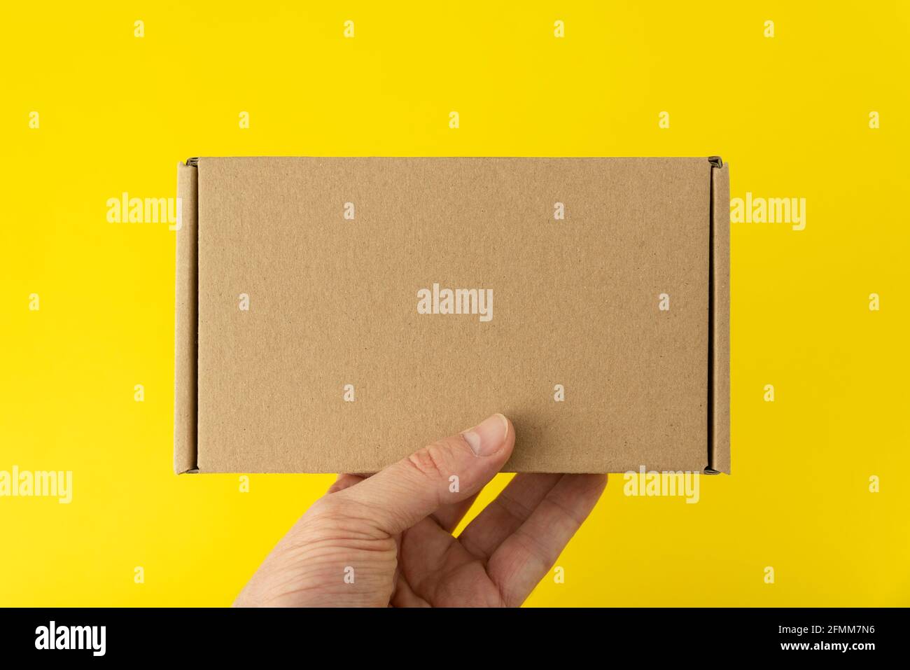 Hand holds rectangular cardboard box, yellow background. Copy space. Mock up Stock Photo